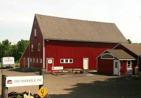 Red barn with a sign reading 'The Paddock Inc.' in a rural setting.